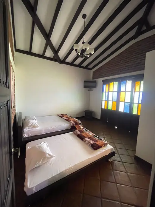 Habitación con dos camas, techo de vigas y ventana con vitrales