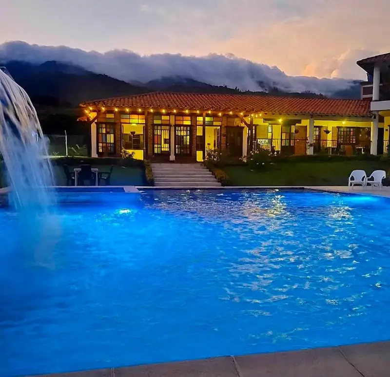 Piscina de la finca al atardecer con la casa principal iluminada